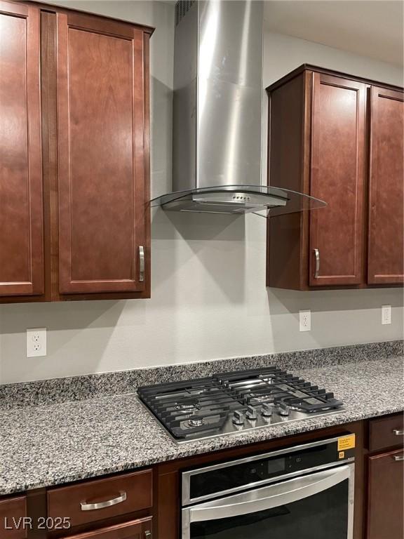 kitchen with stainless steel appliances, wall chimney range hood, and light stone counters