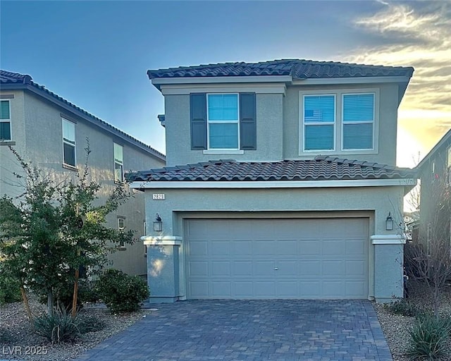 traditional-style house with a garage, a tile roof, decorative driveway, and stucco siding