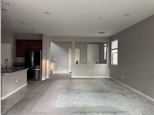 unfurnished living room with baseboards, a sink, visible vents, and light carpet