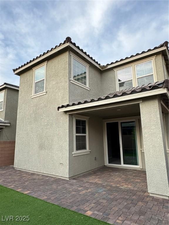 rear view of property featuring stucco siding, a tile roof, fence, and a patio