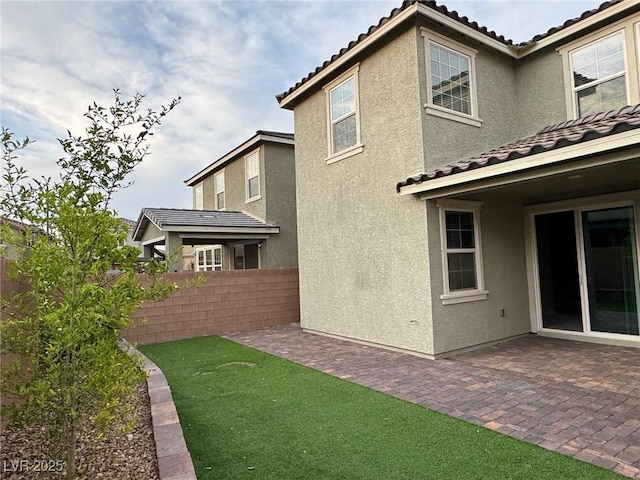 rear view of house with stucco siding, a patio area, a tiled roof, and fence