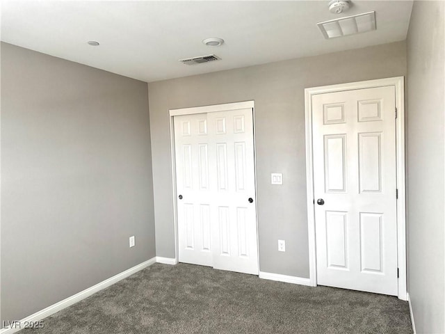 unfurnished bedroom with a closet, dark colored carpet, visible vents, and baseboards