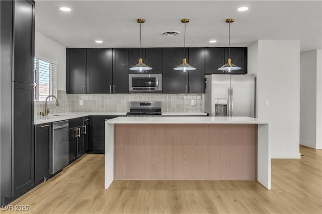 kitchen with light wood finished floors, a sink, a center island, stainless steel appliances, and light countertops