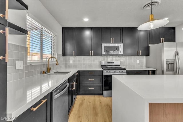 kitchen with light wood-style flooring, a sink, stainless steel appliances, light countertops, and tasteful backsplash