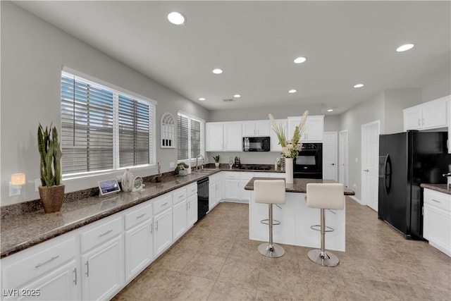 kitchen with white cabinetry, a sink, black appliances, dark stone countertops, and a kitchen bar