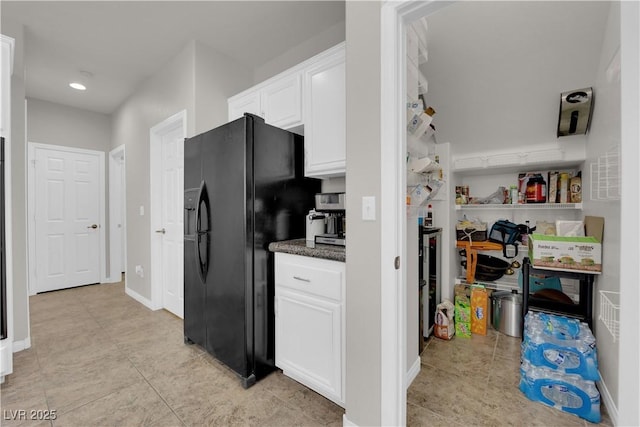 kitchen with light tile patterned floors, black refrigerator with ice dispenser, white cabinetry, dark stone countertops, and baseboards