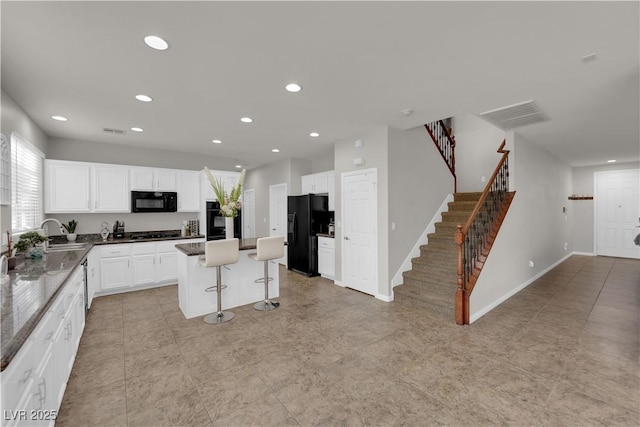 kitchen featuring white cabinets, a kitchen island, a sink, black appliances, and a kitchen bar