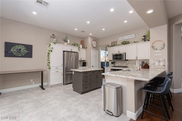 kitchen featuring visible vents, white cabinets, appliances with stainless steel finishes, a kitchen breakfast bar, and a peninsula