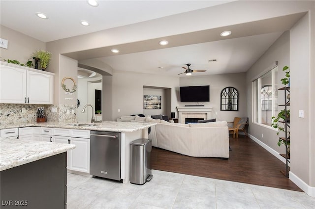 kitchen with white cabinets, dishwasher, open floor plan, light stone countertops, and a sink