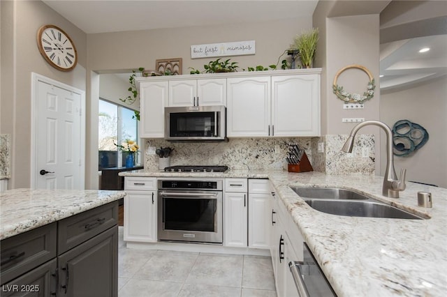 kitchen featuring appliances with stainless steel finishes, white cabinetry, a sink, and light stone countertops