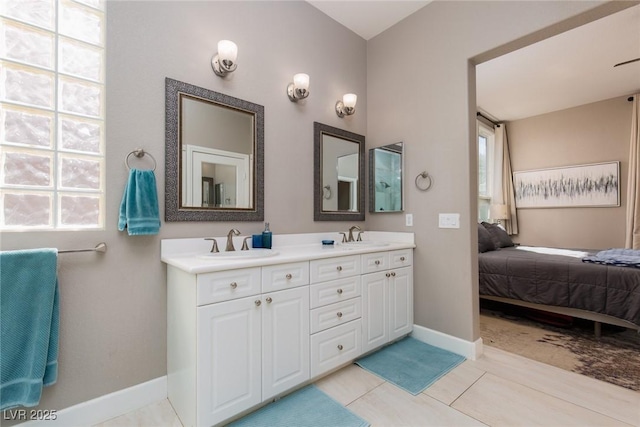 bathroom with ensuite bathroom, double vanity, a sink, and baseboards