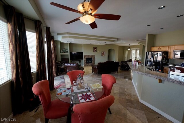 dining room with arched walkways, a fireplace, baseboards, and a ceiling fan