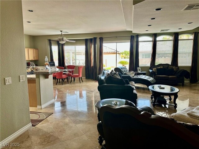 living area with visible vents, baseboards, ceiling fan, and a textured wall