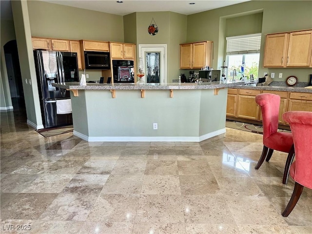 kitchen with a breakfast bar area, light brown cabinets, and black appliances