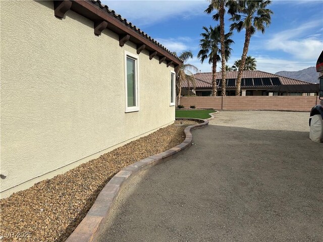 view of side of property featuring stucco siding, a tile roof, and fence