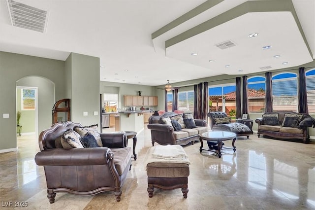 living area with arched walkways, a ceiling fan, visible vents, and baseboards