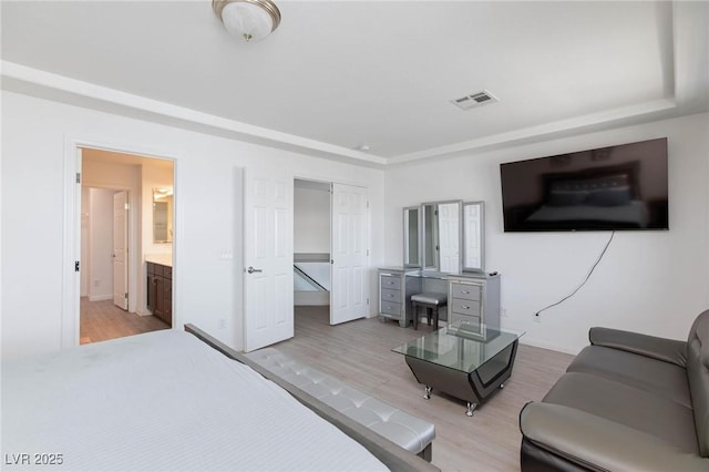 bedroom with light wood-style floors, visible vents, baseboards, and ensuite bathroom