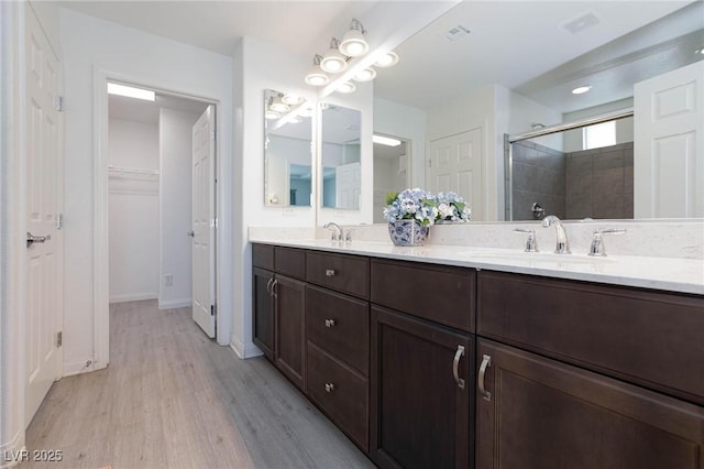 bathroom featuring wood finished floors, a sink, a spacious closet, a shower stall, and double vanity