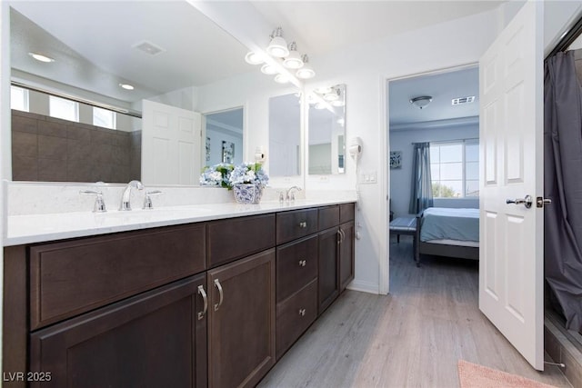 ensuite bathroom featuring double vanity, visible vents, a sink, ensuite bath, and wood finished floors