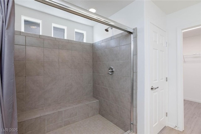 full bathroom featuring a stall shower, a walk in closet, and wood finished floors