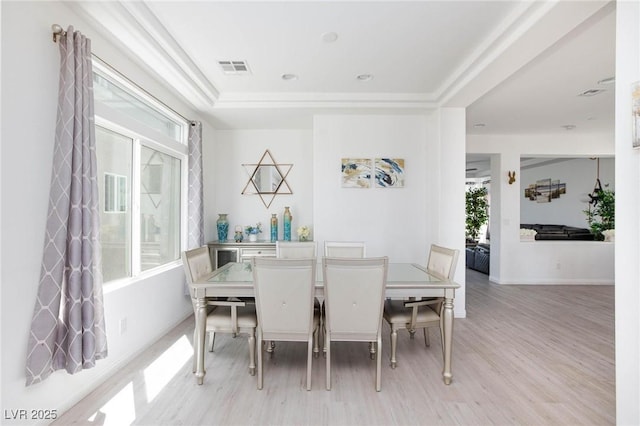 dining space featuring a tray ceiling, visible vents, light wood-style flooring, and baseboards