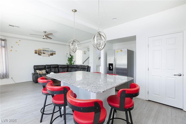 kitchen featuring light wood-style flooring, open floor plan, stainless steel refrigerator with ice dispenser, a kitchen bar, and decorative light fixtures