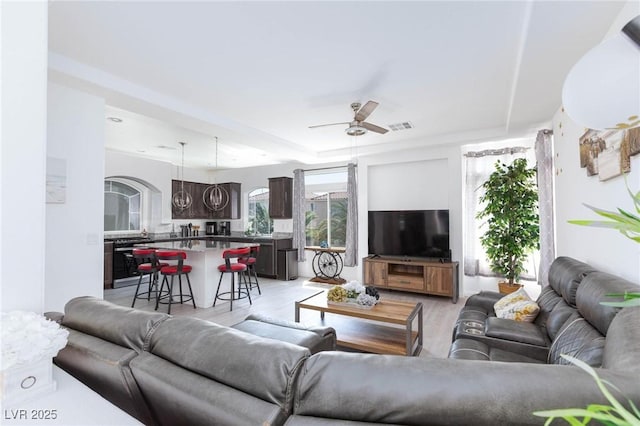 living room featuring light wood-type flooring, visible vents, and ceiling fan