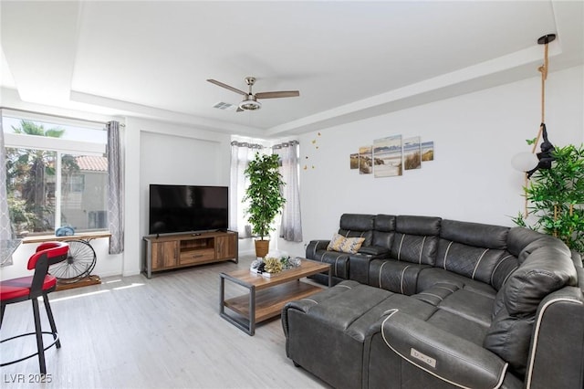 living room with wood finished floors, a raised ceiling, visible vents, and a ceiling fan