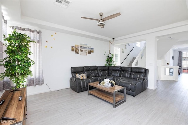 living room with stairway, light wood-style flooring, visible vents, and ceiling fan