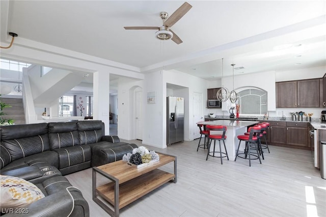 living room with ceiling fan, light wood finished floors, and arched walkways