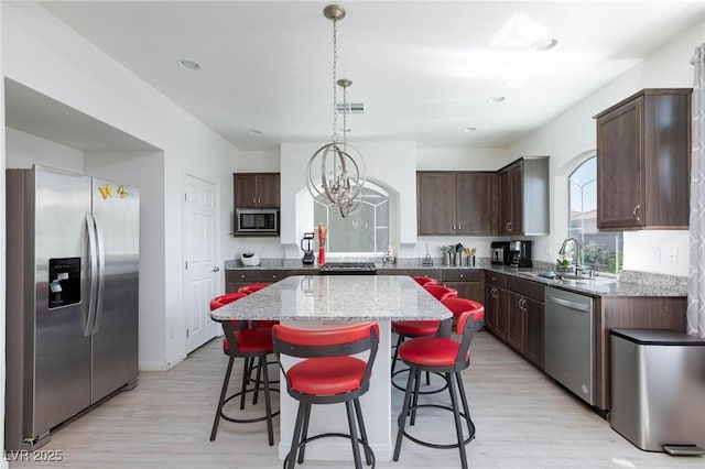 kitchen with dark brown cabinetry, stainless steel appliances, a sink, and a center island