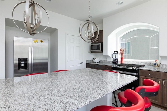 kitchen featuring light stone counters, a notable chandelier, appliances with stainless steel finishes, dark brown cabinetry, and a kitchen bar