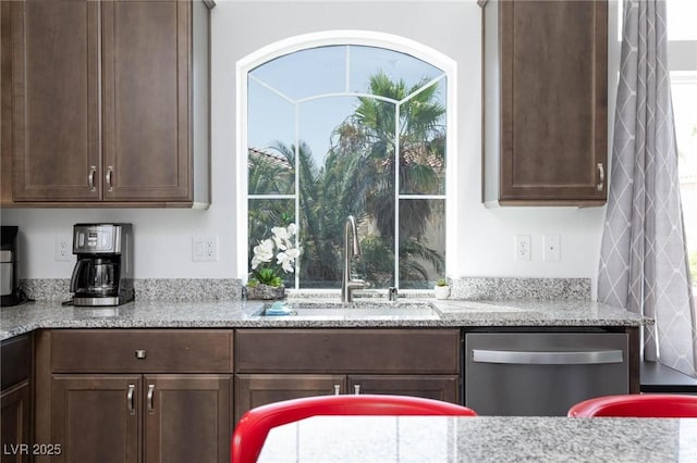 kitchen featuring a sink, light stone countertops, dark brown cabinets, and stainless steel dishwasher