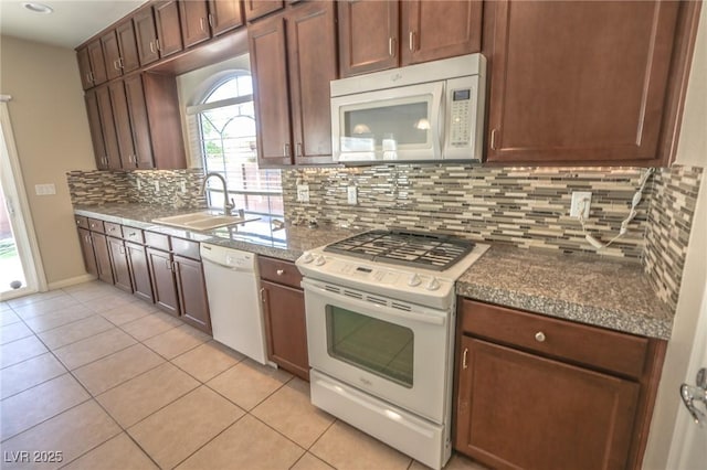 kitchen featuring white appliances, dark stone counters, decorative backsplash, a sink, and light tile patterned flooring