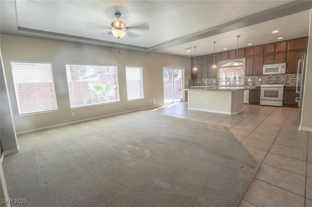 unfurnished living room with baseboards, light tile patterned flooring, a raised ceiling, and light colored carpet