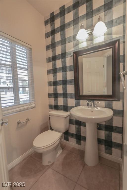 half bathroom featuring toilet, a sink, tile patterned flooring, baseboards, and wallpapered walls