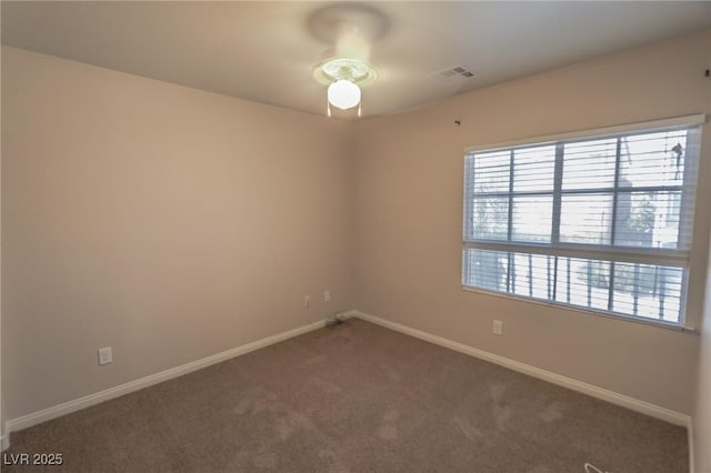 spare room with plenty of natural light, visible vents, dark carpet, and baseboards