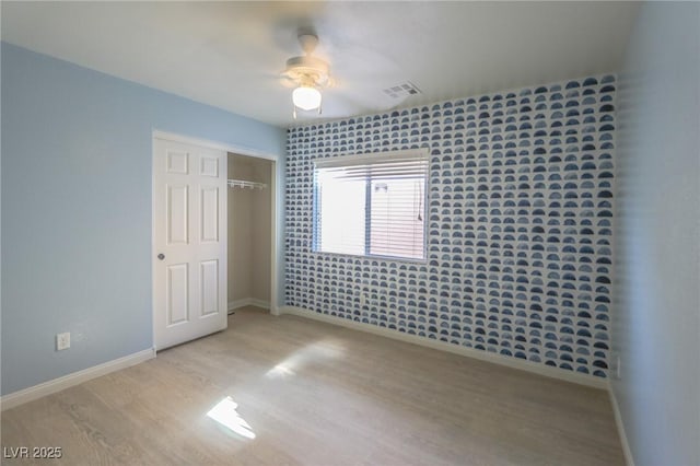 unfurnished bedroom featuring a ceiling fan, baseboards, visible vents, light wood-style floors, and a closet