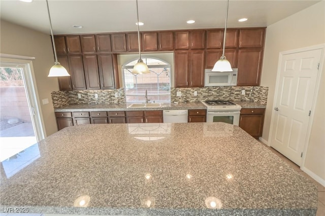 kitchen featuring white appliances, decorative backsplash, light stone counters, decorative light fixtures, and a sink