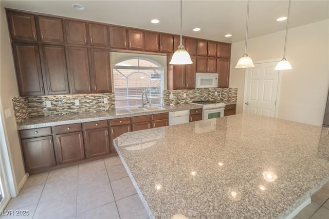 kitchen featuring white appliances, a spacious island, light stone counters, pendant lighting, and a sink