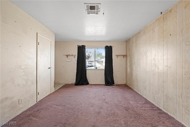 spare room featuring wooden walls, visible vents, and light carpet