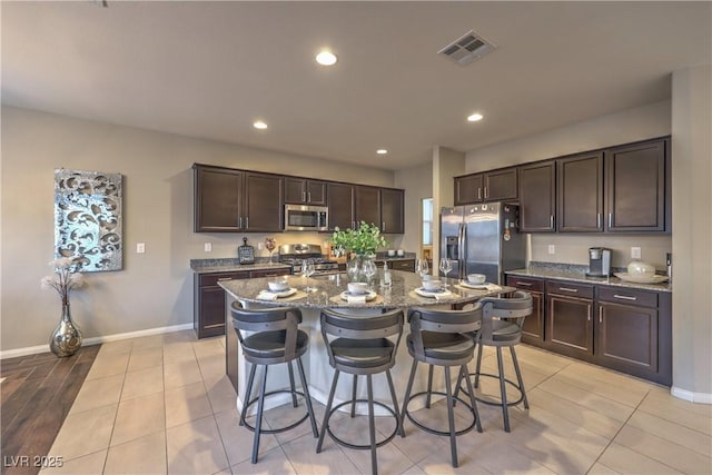 kitchen with stainless steel appliances, a breakfast bar, dark brown cabinetry, and dark stone countertops