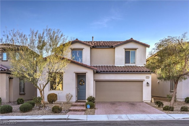 mediterranean / spanish home with stucco siding, a tile roof, decorative driveway, and a garage