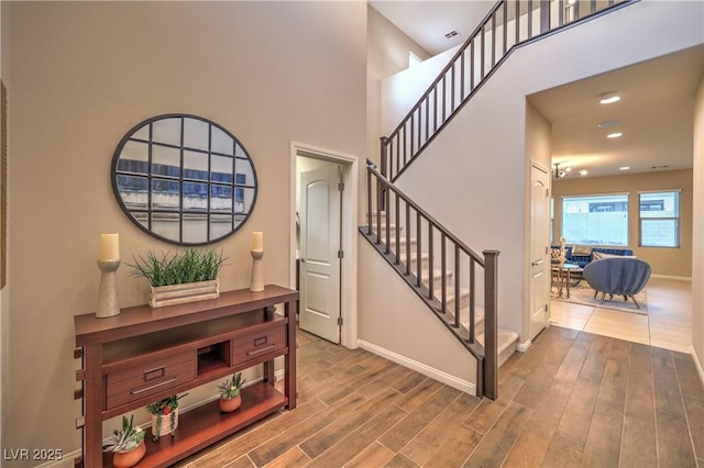 interior space featuring baseboards, recessed lighting, a towering ceiling, wood finished floors, and stairs