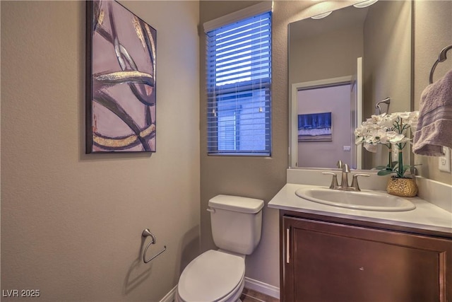 half bath with baseboards, vanity, and toilet
