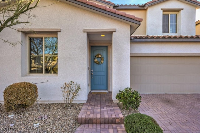 property entrance with a garage, a tiled roof, decorative driveway, and stucco siding