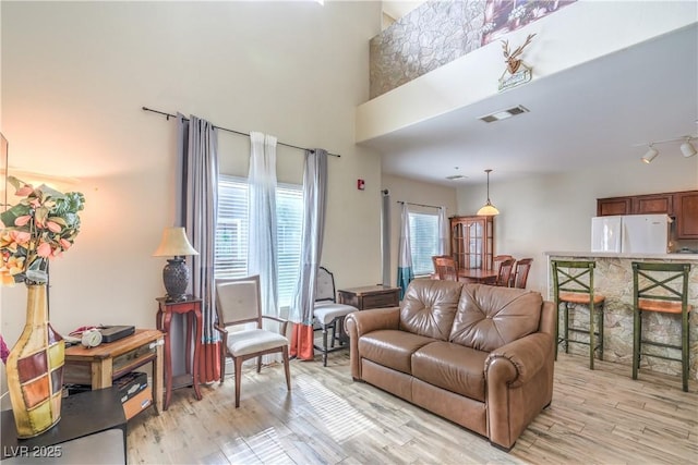 living room with a high ceiling, visible vents, and light wood finished floors