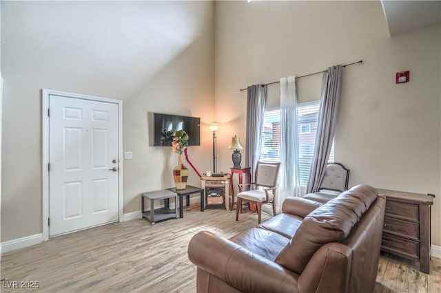 living area with a towering ceiling, light wood finished floors, and baseboards