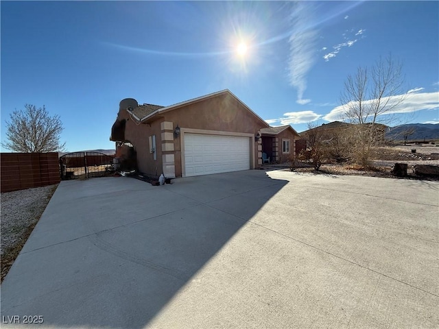 view of property exterior with driveway, a garage, fence, a mountain view, and stucco siding