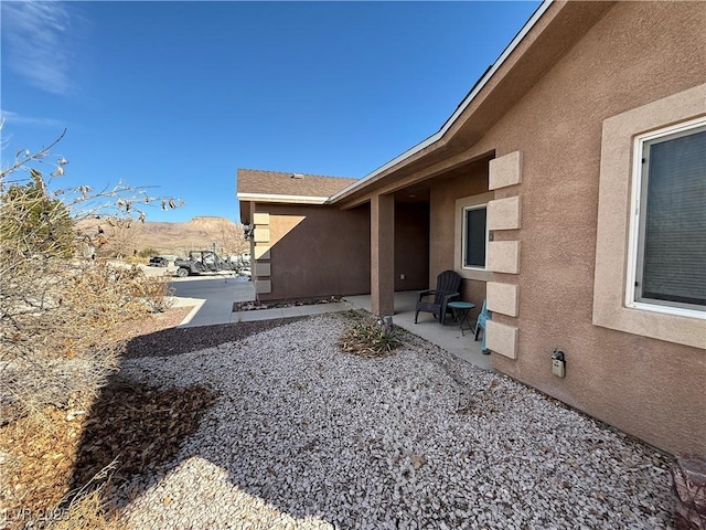 view of side of home featuring a mountain view, a patio, and stucco siding